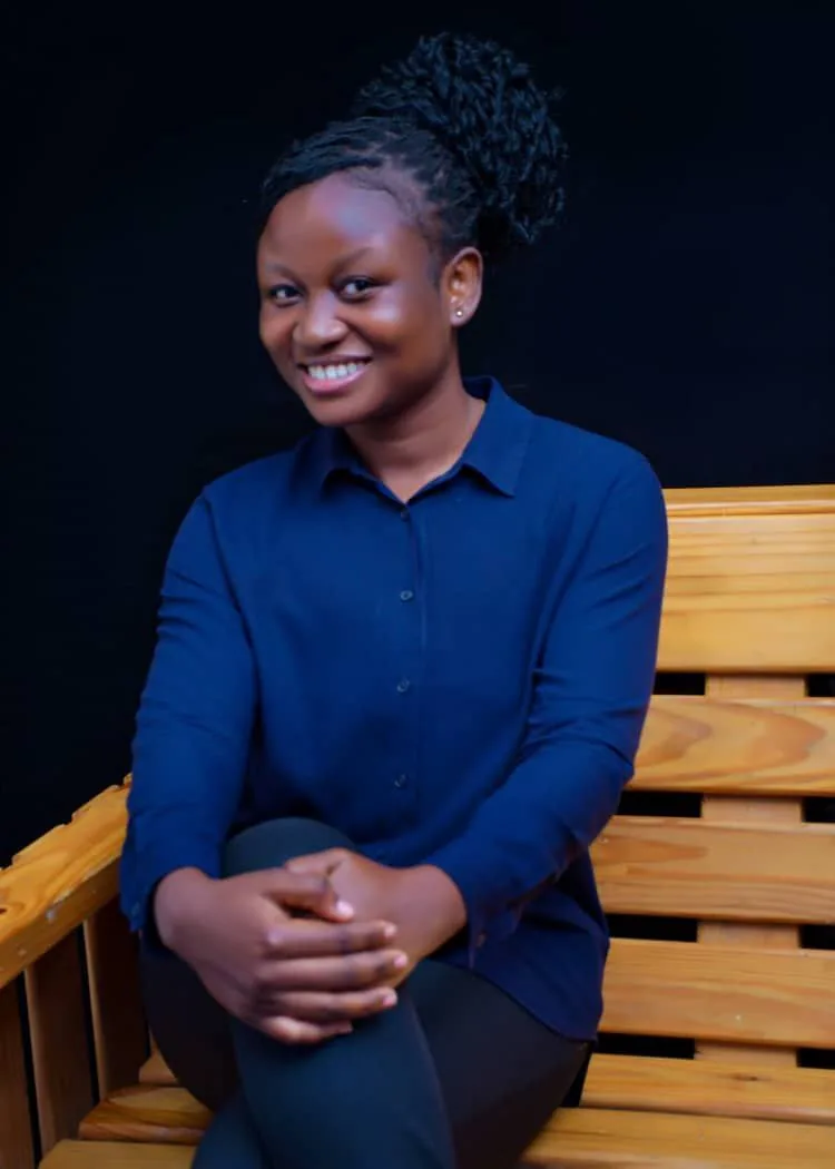 Portrait of Priscilla Nana Yaa Nti, Product Manager, smiling and seated on a wooden bench in a navy blouse